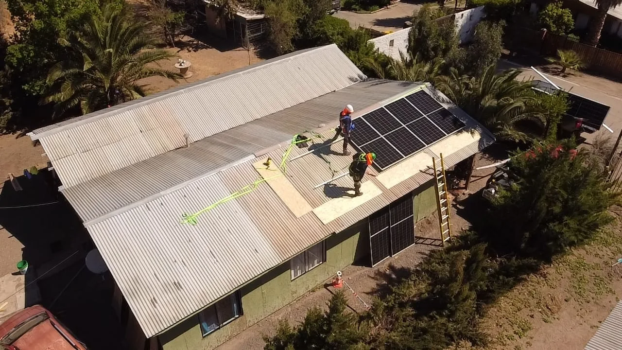 Vista aérea de una vivienda de Tiltil con instaladores montando los módulos fotovoltaicos sobre la cubierta