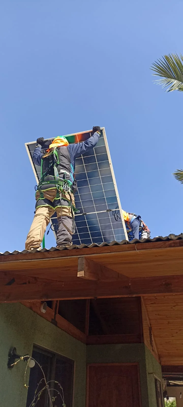 Dos operarios asegurados izando un módulo fotovoltaico hasta la cubierta de una vivienda