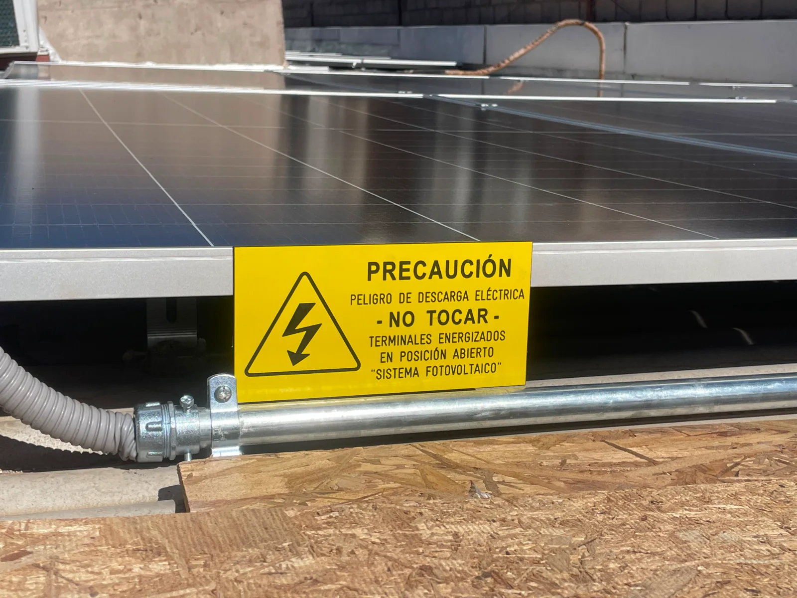 Detalle de canalización metálica y señalética de precaución bajo los módulos en cubierta