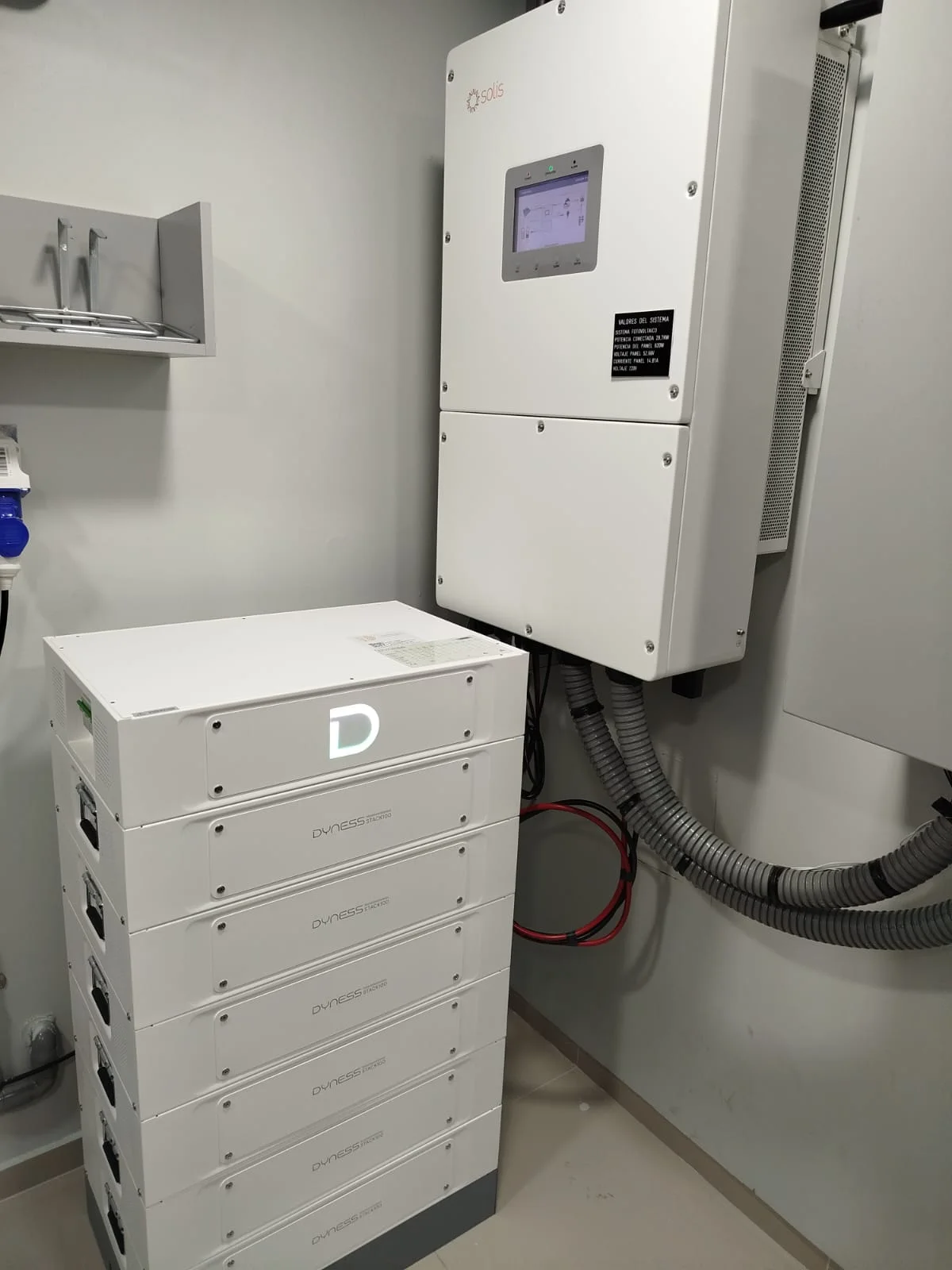 Sala técnica con inversor híbrido Solis montado en muro y banco de baterías Dyness apilado